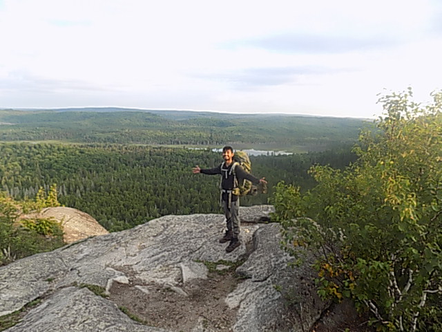 Ibrahim on a rocky summit with a backpack, vast Canadian wilderness behind him